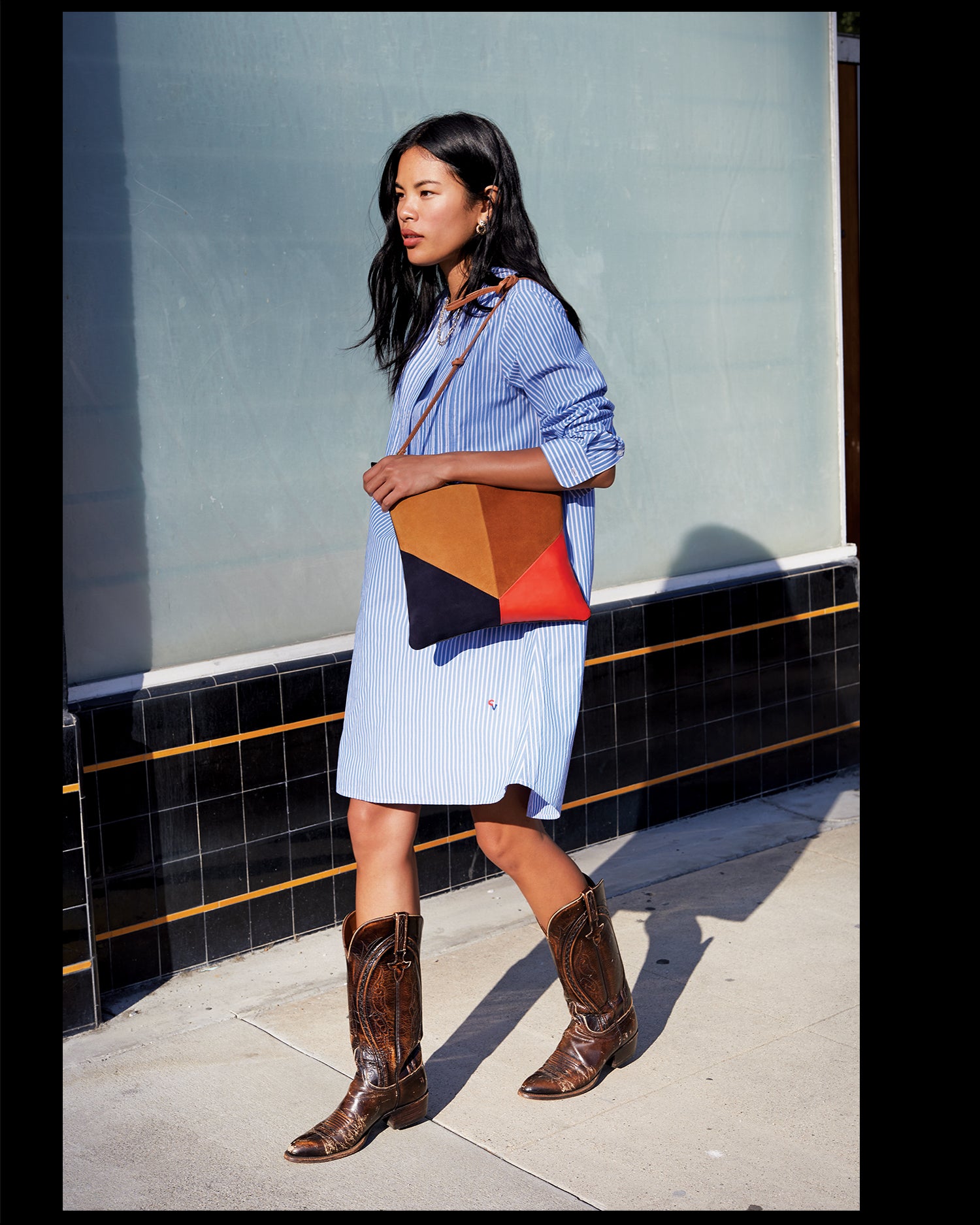 Sandra wearing the Blue & Cream Stripe Le Tux Dress and carrying the Suede & Nappa Patchwork Foldover Clutch with Tabs over her shoulder as she has our Cuoio Thin Knotted Shoulder Strap attached to the clutch.