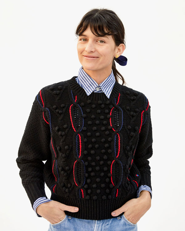 danica wearing the Black with red and navy chains Drop Shoulder Sweater over a collared shirt with her hands in the pockets of her jeans