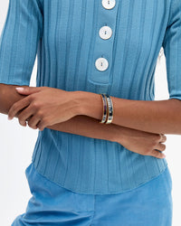 A close-up of a person wearing a blue ribbed short-sleeve top with white buttons and wearing two stacked Le Bangles.