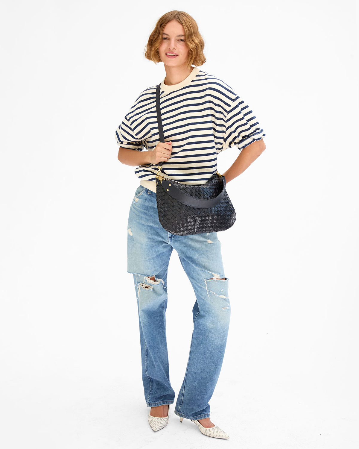 Model wearing the cream and navy Short Sleeve Oversized Sweatshirt, distressed light blue jeans, and white shoes and carrying the Twilight Diagonal Woven Moyen Messenger as a crossbody bag using the crossbody strap the bag comes with. 