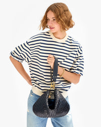 Model carrying the Model wearing the Twilight Diagonal Woven Moyen Messenger as a top handle bag by cinching the bag using the Shoulder Strap.