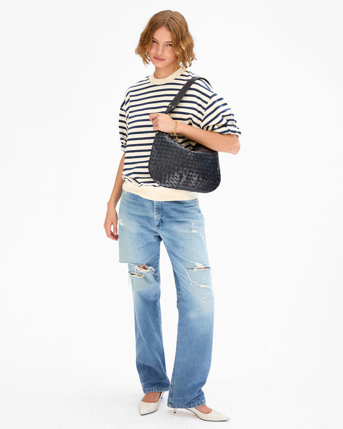 Model wearing the cream and navy Short Sleeve Oversized Sweatshirt, distressed light blue jeans, and white shoes and carrying the Twilight Diagonal Woven Moyen Messenger over her shoulder. 