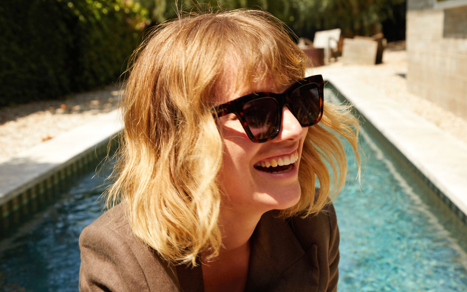 Lou wearing our Tortoise Heather Sunglasses and smiling as she's in front of a pool.