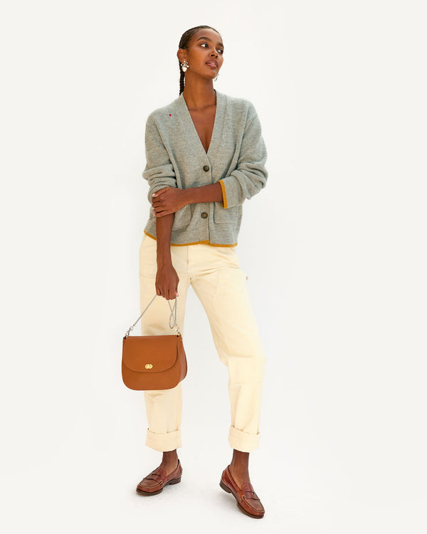Jordan in the oscar cardigan with white pants and brown loafers. she's holding the cuoio turnlock louis by the silver Snake Chain Shoulder Strap