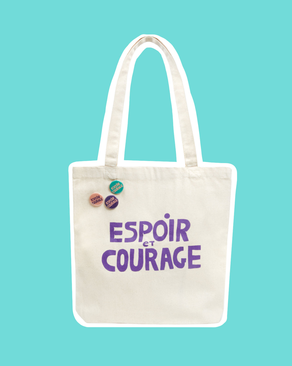 CV x Giffords Canvas Tote with Pins that says Espoir Et Courage in purple writing. The Tote is sitting in front of a turquoise background.
