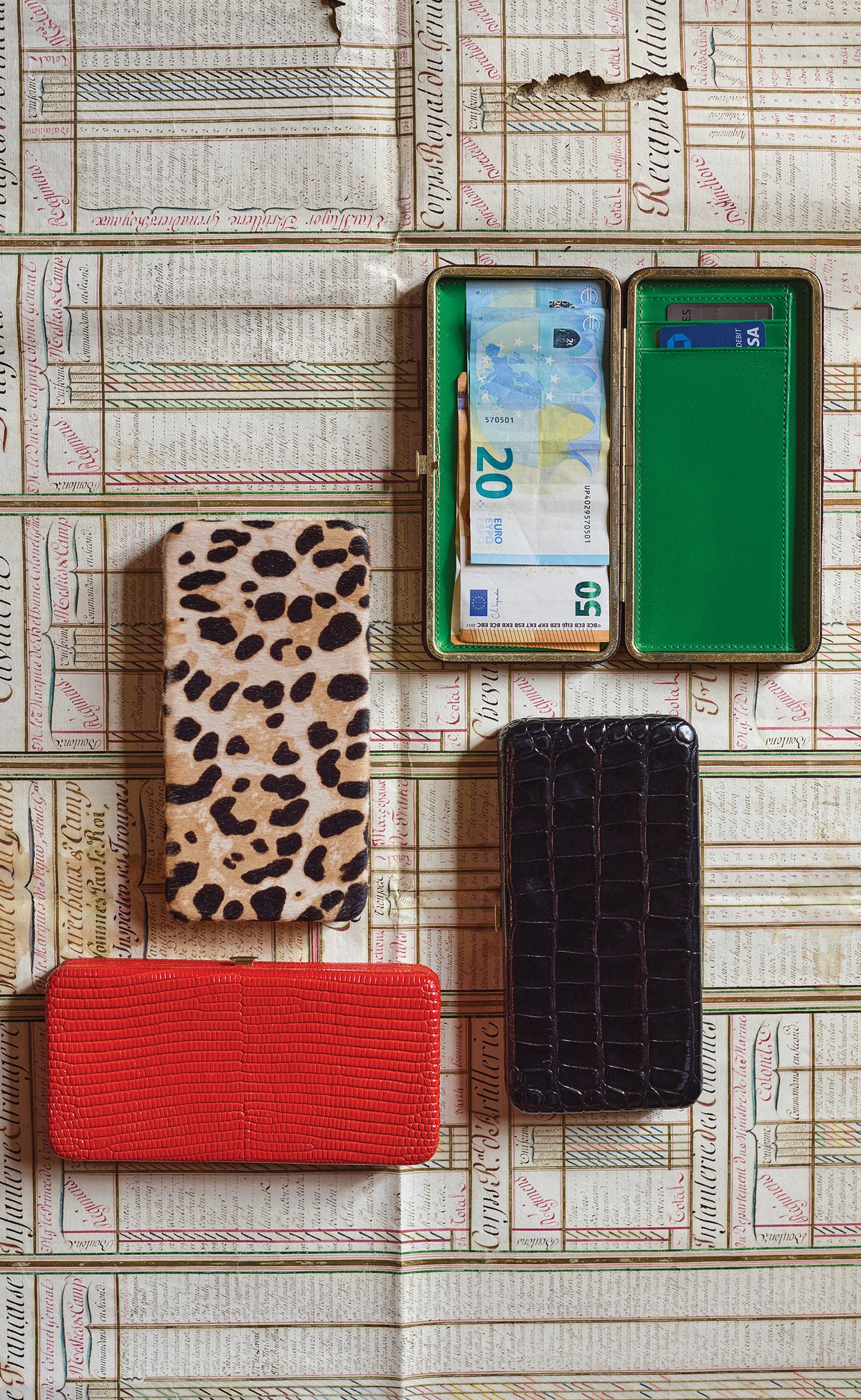 Le Tabacs in Red Embossed Lizard, Snow Leopard, Black Croco, and Truffle Suede which is open and is showing its green interior with foreign money inside. 