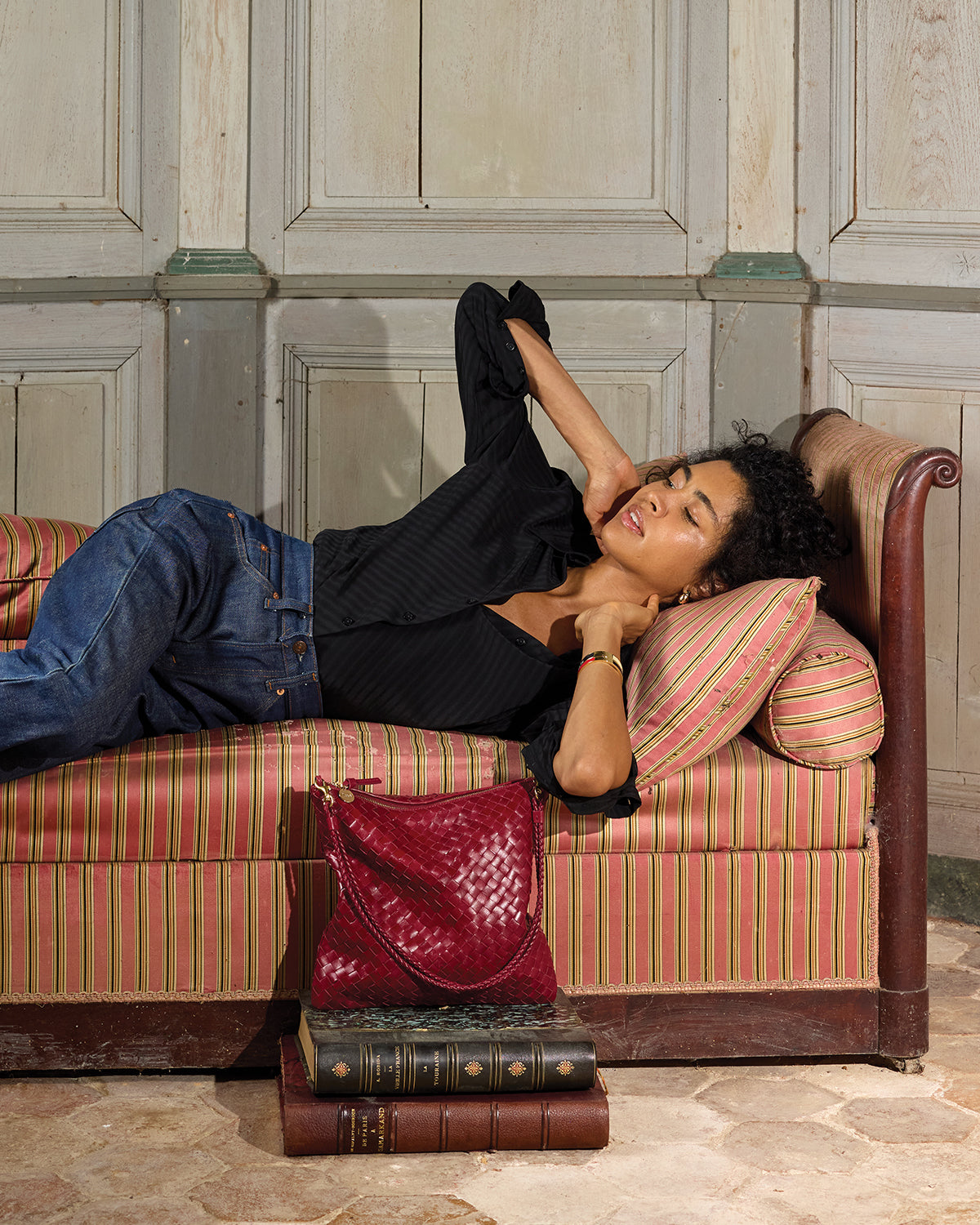 Model laying down on a bed with the Garnet Diagonal Woven Foldover Clutch with Strap. 