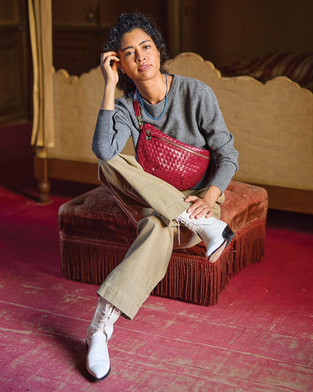 Model sitting down and carrying the Garnet Diagonal Woven Grande Fanny across her chest. 