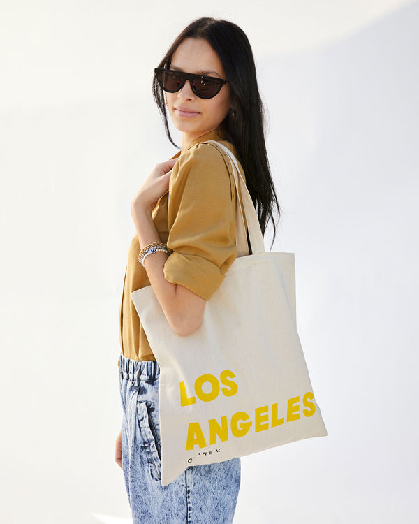 Aurelia is wearing acid wash jeans and a tan sweater with the Natural Oui Canvas Store Tote on her shoulder. 
