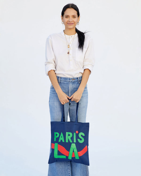 Aurelia wearing wide leg jeans with a button up white top. she's holding the  Navy Paris L.A. Canvas Store Tote out in front of her with both hands
