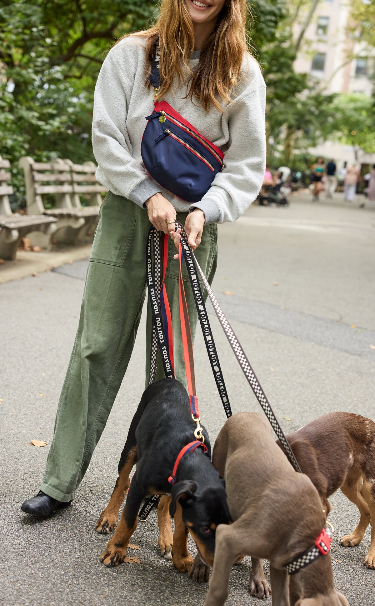 Model wearing the CV x The Dogist Grande Fanny Sportif as a crossbody while walking three dogs using an assortment of Clare V. x The Dogist leashes. 