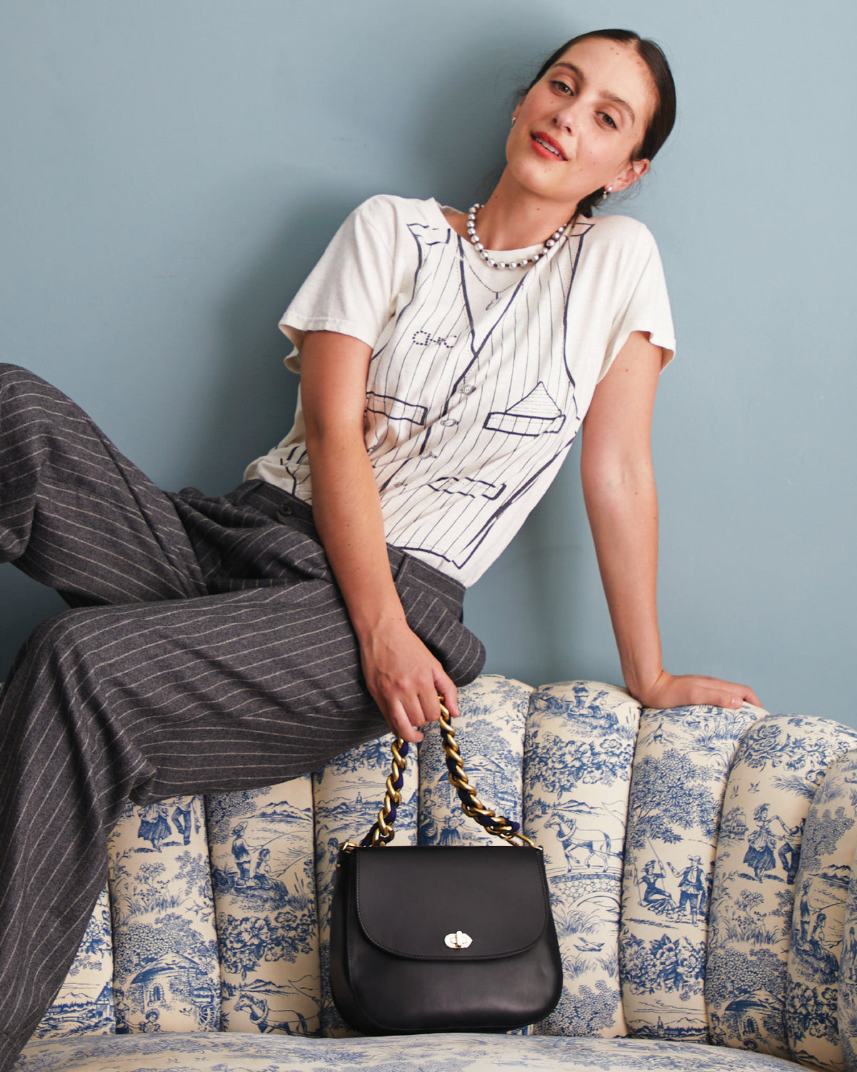 Frannie wearing the Classic Te in Cream with Trope L'Oeil Vest and holding a Black Turnlock Louis in Black with the Vintage Brass with Navy Grosgrain Shortie Strap attached to it. 
