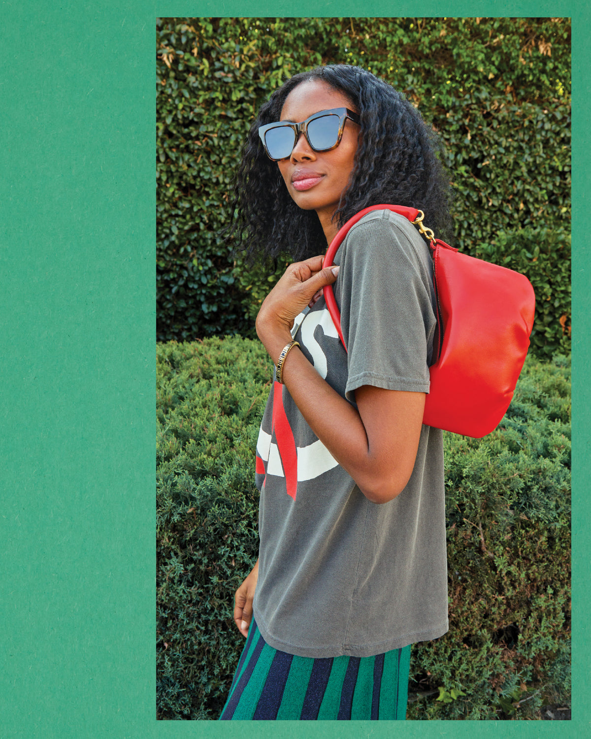 Mecca wearing the Original Tee in Faded Black with Paris LA printed on it with the Héloïse Accordion Skirt. Mecca is carrying the Rouge Nappa Luxe Petit Moyen over her shoulder and is also wearing the Tortoise Heather Sunglasses.
