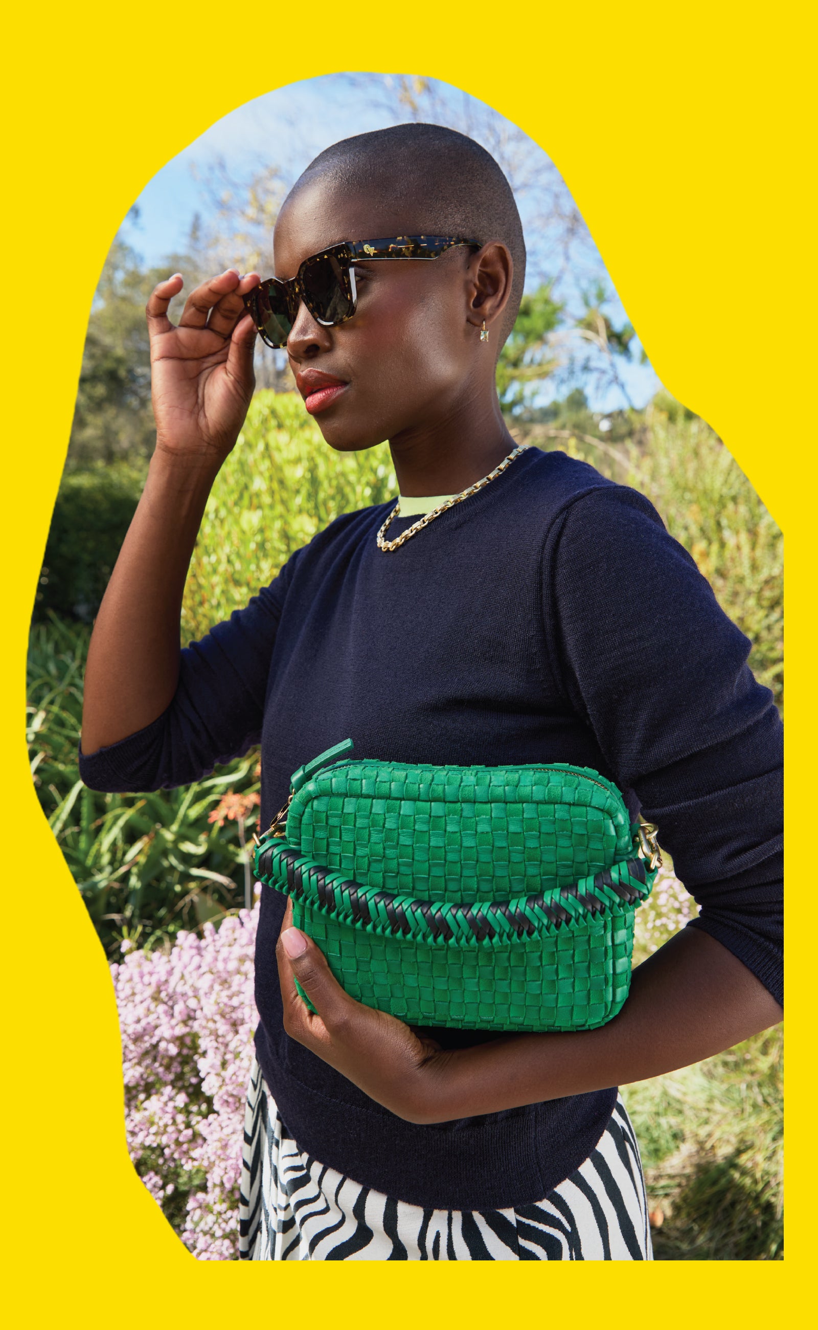 Model wearing the Zebra Tortoise James Sunglasses and holding the Grass Woven Midi Sac with Green Apple Braided Top Handle.