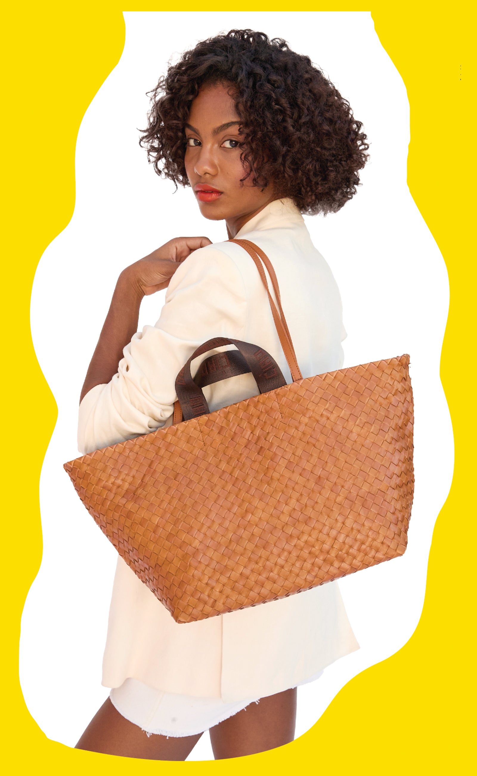 Model wearing a cream blazer and carrying the Natural Woven Diagonal Bateau Tote over her shoulder. 