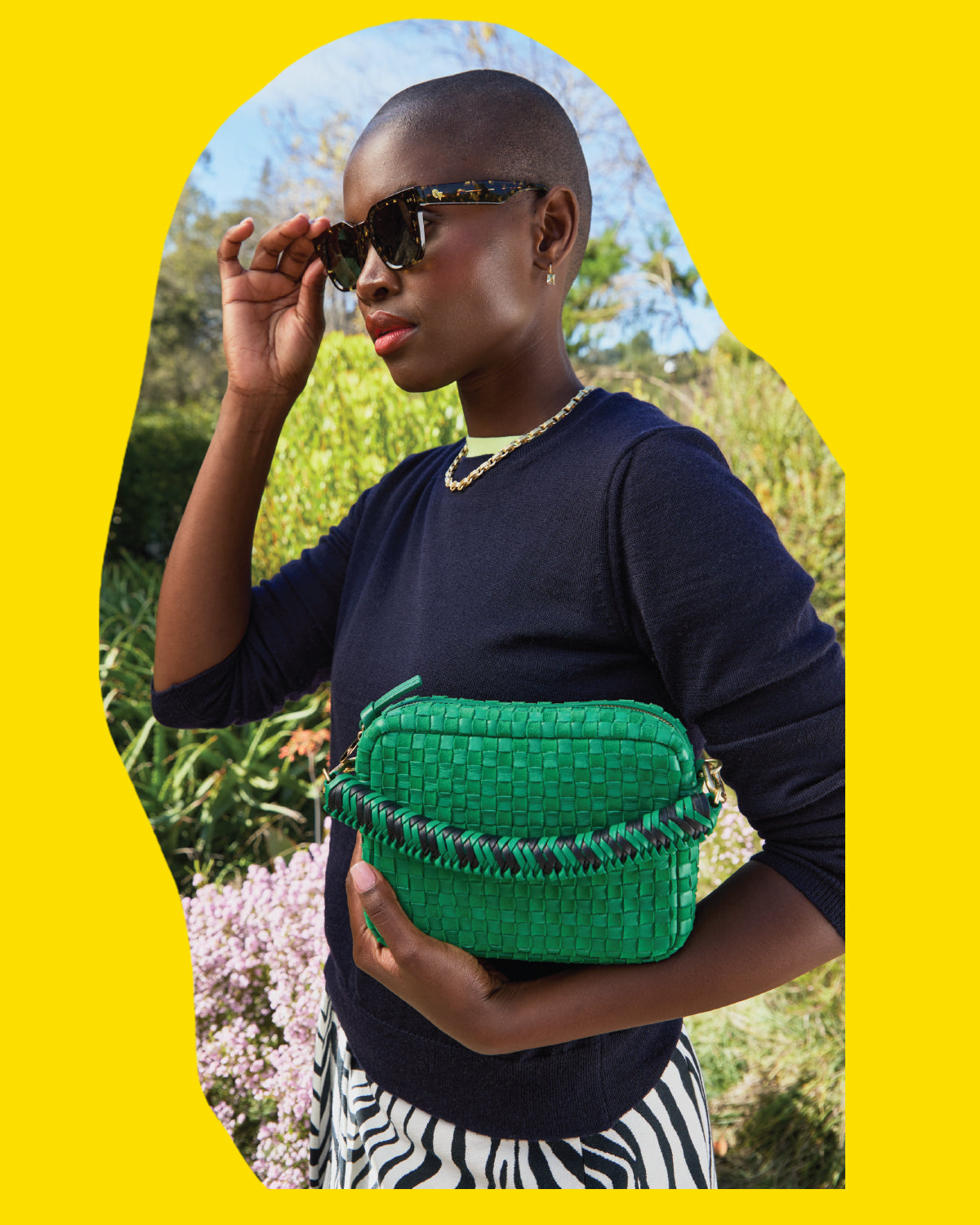 Model wearing the Zebra Tortoise James Sunglasses and holding the Grass Woven Midi Sac with Green Apple Braided Top Handle.