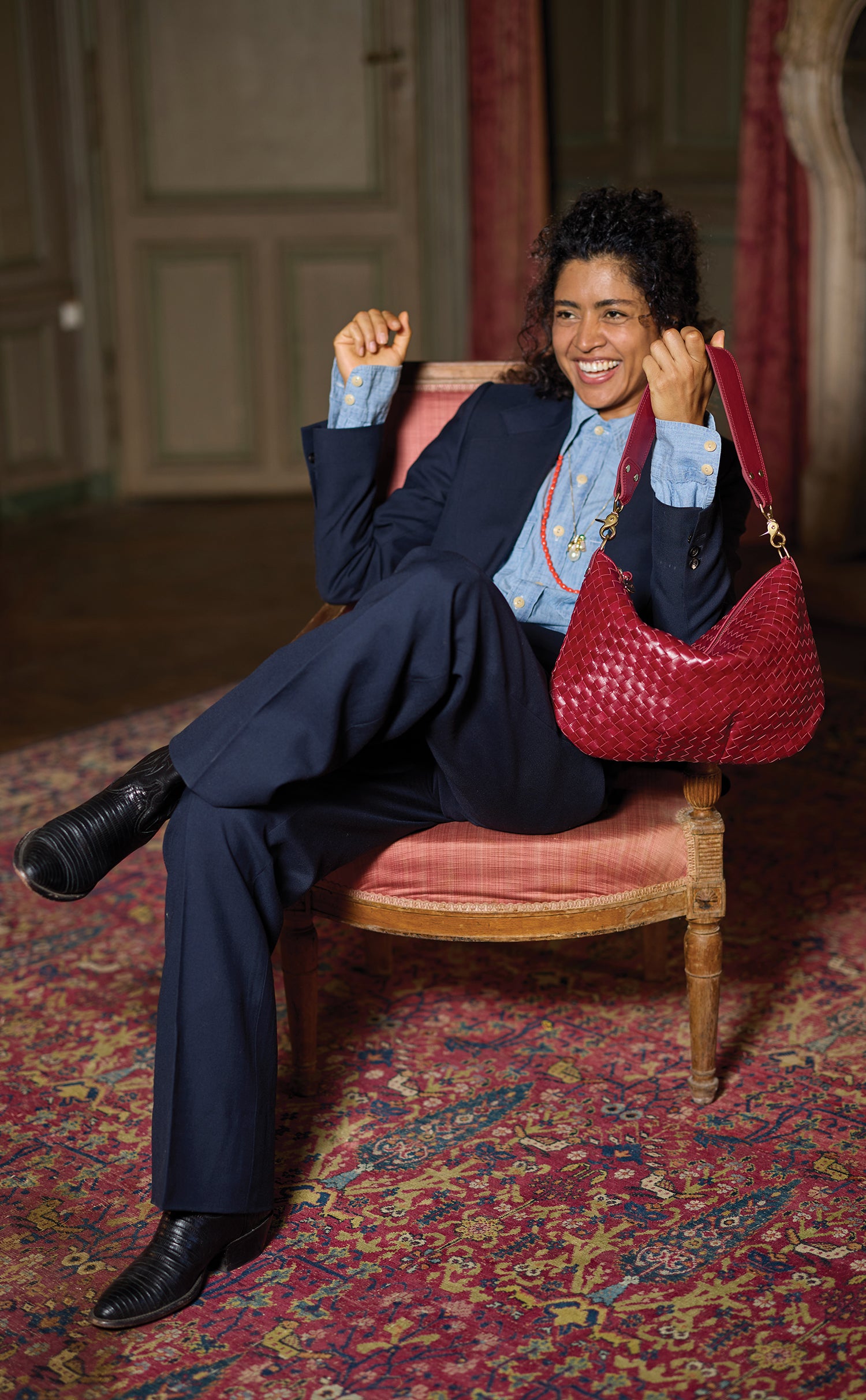 Model sitting on a chair and holding the Garnet Diagonal Woven Moyen Messenger. 