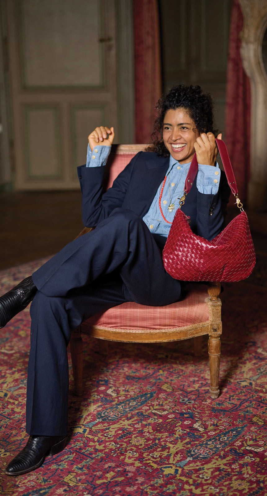 Model sitting on a chair and holding the Garnet Diagonal Woven Moyen Messenger. 