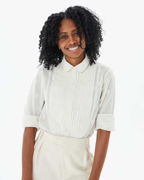 Mecca from the waist up in the Cream Heart Coupé Anette Tuxedo Shirt with white front pleated slacks and her arms at her side