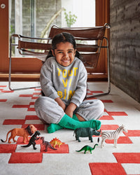 Child sitting on the Cream & Poppy Rug with a chair in the background and some toy animals 