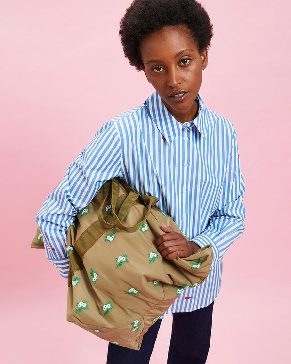 Model wearing the Blue & Cream Stripes w/ Poppy Lips Button Up Shirt and carrying the Khaki Bomber Jacket in her arms
