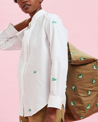 Model wearing the White w/ Green Embroidered Ciao Button Up Shirt with the Khaki Bomber Jacket being held over her shoulder