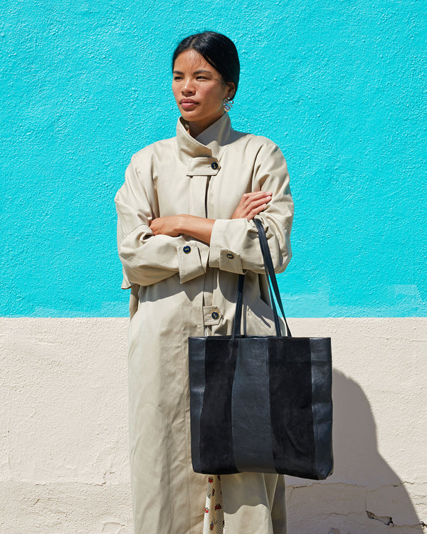 Sandra wearing a tan trench coat with the Black Suede & Nappa Bande Tote resting on her forearm