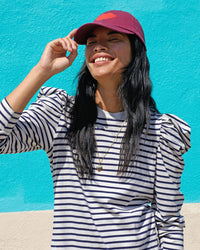 Sandra smiling and touching the brim of the Oxblood with Lips Baseball Hat