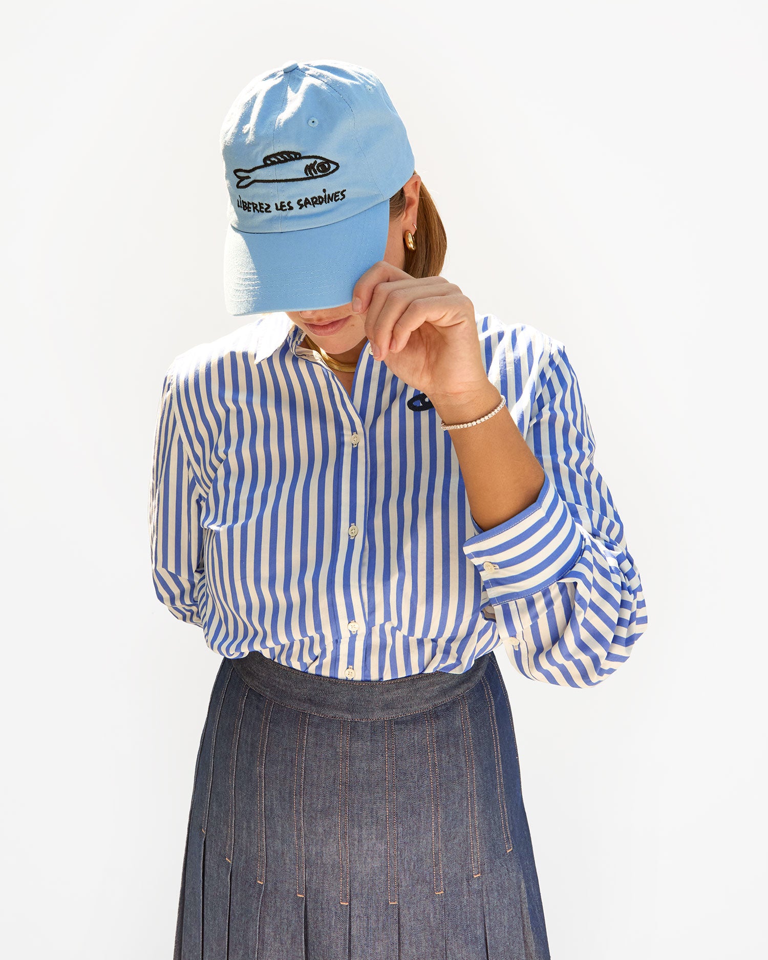 Sonnie wearing the Sky Blue Liberez Les Sardines Baseball Hat with a striped shirt and a pleated skirt