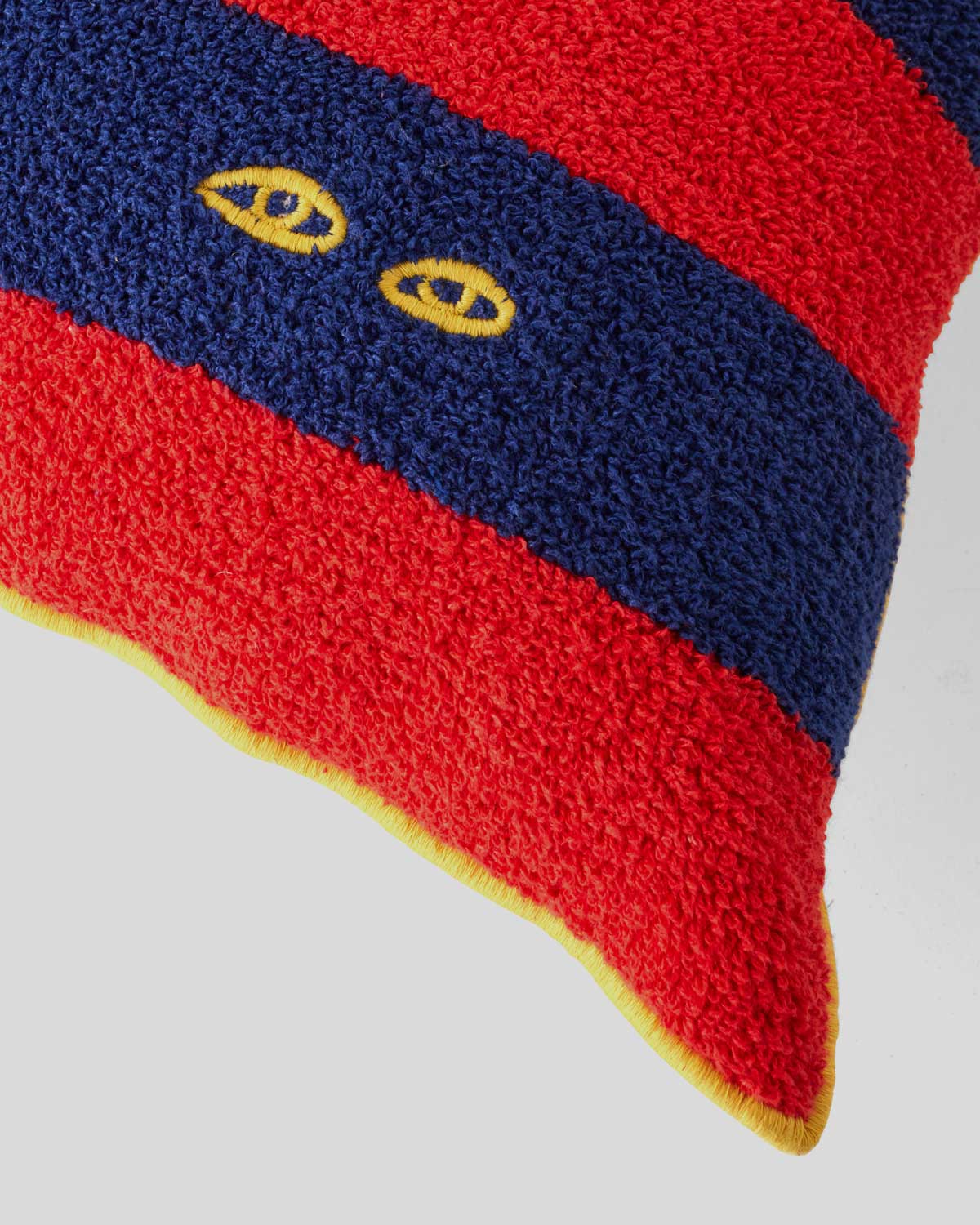 close up of the eyes embroidery on the corner of the Navy & Poppy Stripes w/ Yellow Eyes Coussin