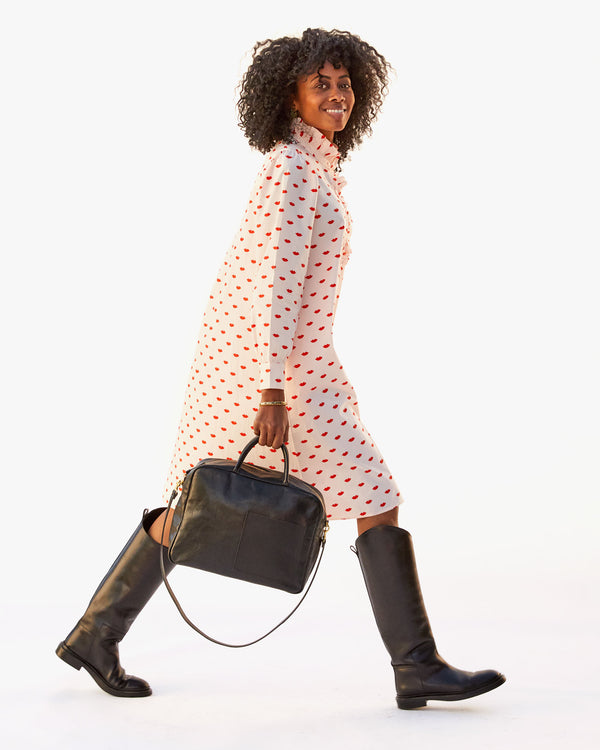 Mecca taking a big step in the Eleanor Dress in Blush w/ Lips while holding the black Claude bag