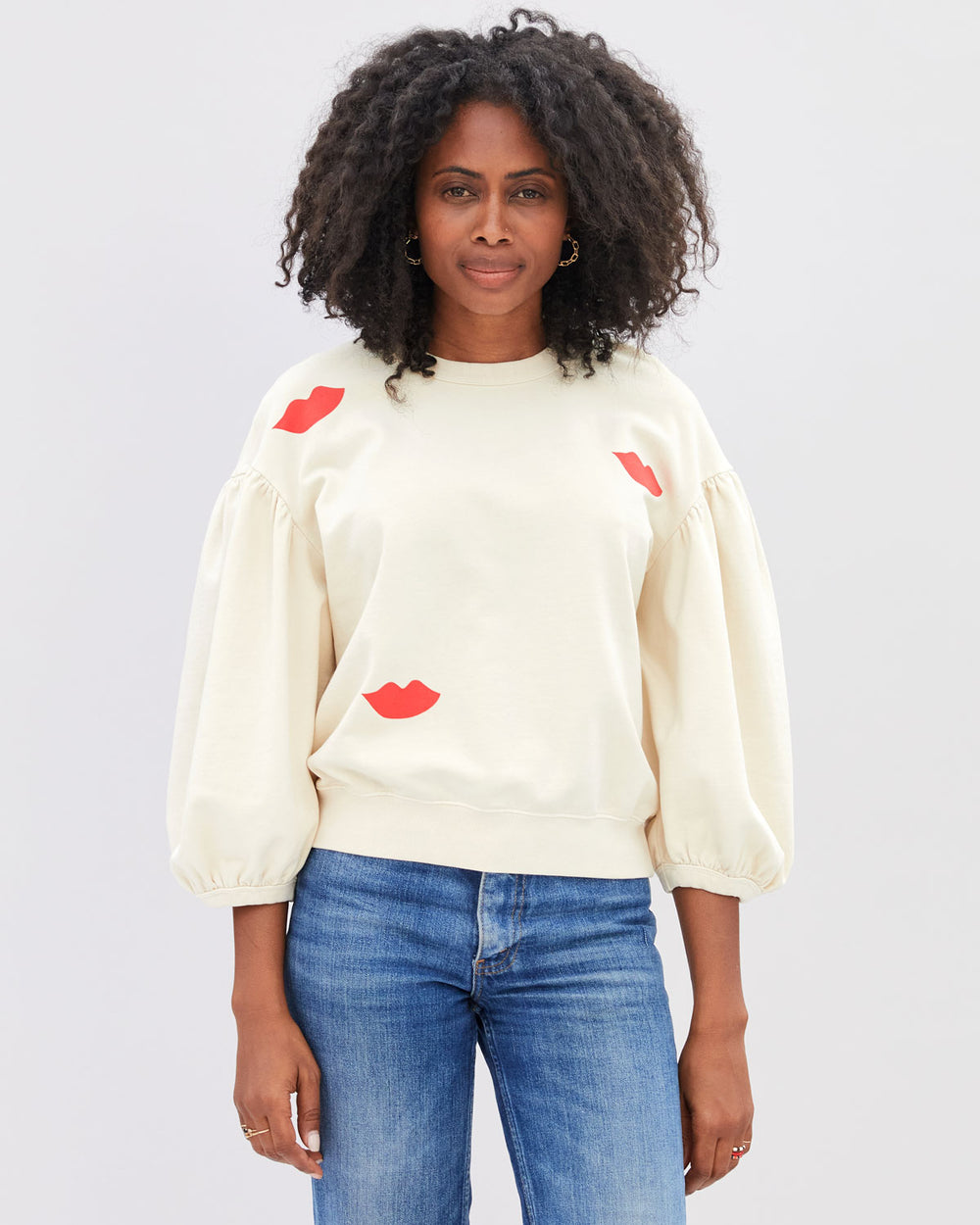 Mecca wearing the Cream with Lips Drop Shoulder Sweatshirt untucked with blue denim jeans.