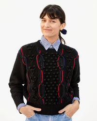 danica wearing the Black with red and navy chains Drop Shoulder Sweater over a collared shirt  with her hands in the pockets of her jeans