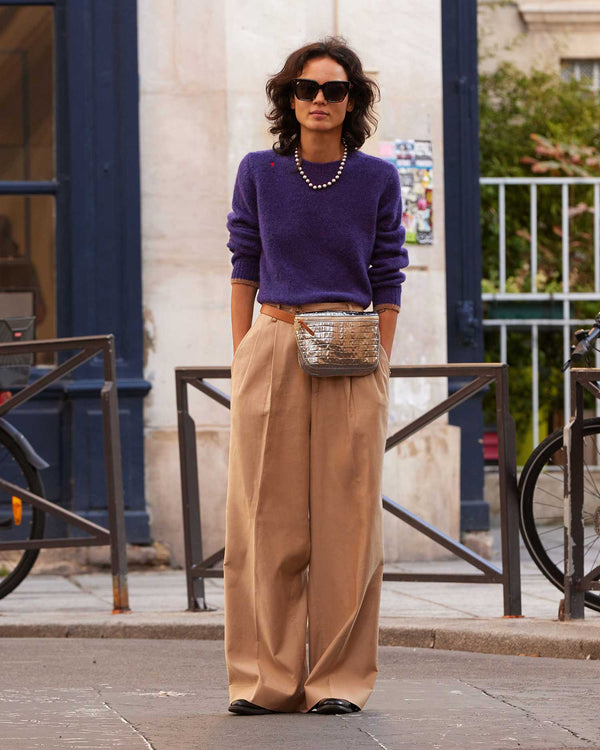 Gabrielle standing with her hands in her pockets in the Sea Urchin Elsa Sweater with tan pleated pants and the silver croco fanny pack around her waist