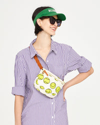 Athena wearing the Natural with Tennis Balls Fanny Pack across her chest. she has on a striped button up and a visor