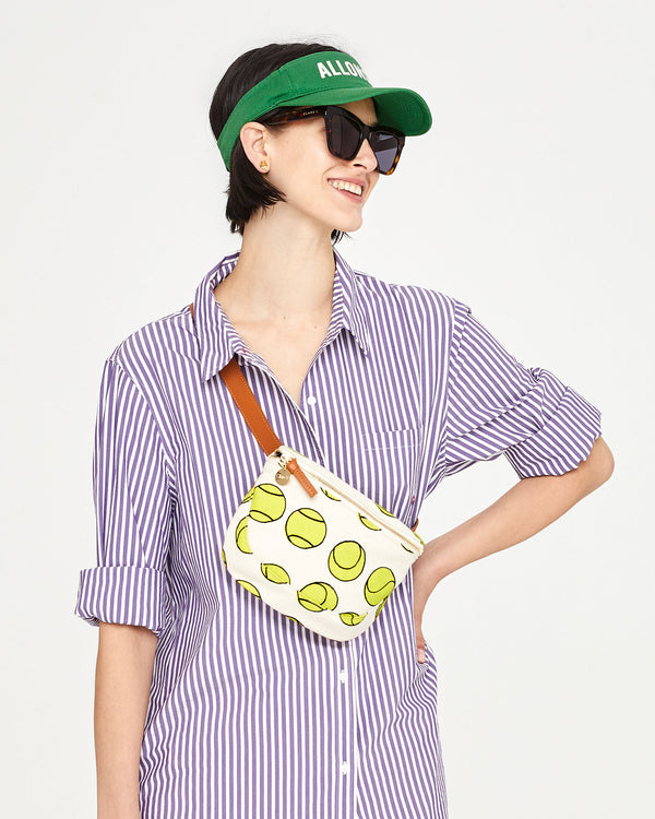Athena wearing the Natural with Tennis Balls Fanny Pack across her chest. she has on a striped button up and a visor