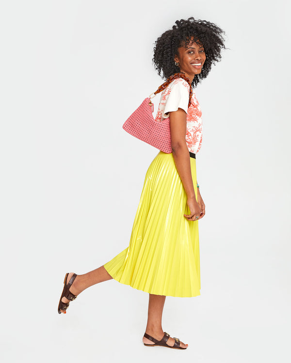 Mecca carrying the unlined Petal Rattan Flat Clutch with Tabs with the Tortoise Resin Shortie Strap over her shoulder.  Mecca is wearing the Classic Tee in Cream w/ Bright Poppy St. Calais Toile with a bright yellow pleated skirt.
