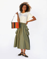 Mecca in a tshirt and an army green skirt holding a flat clutch with tabs by the Black Thin Knotted Shoulder Strap