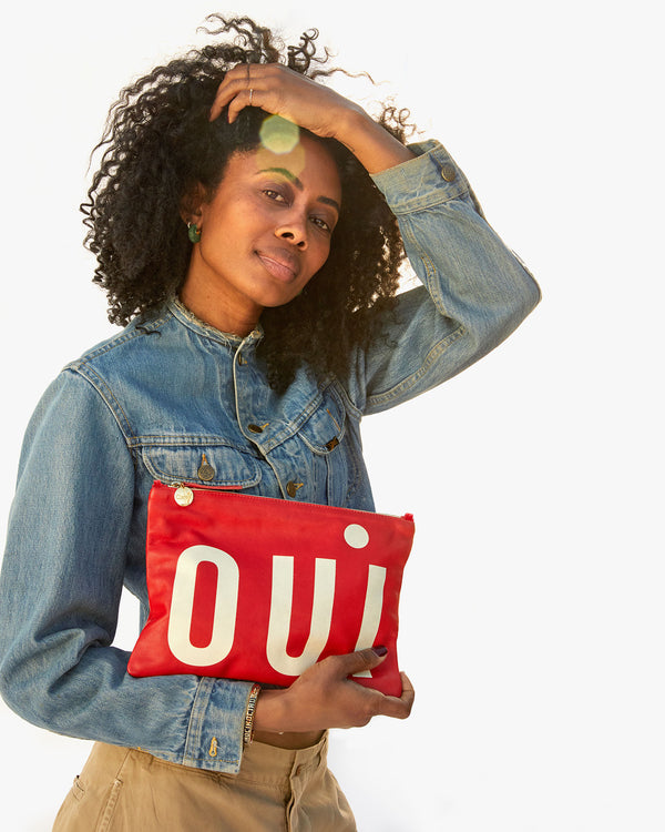 Mecca carrying the Cherry Red Oui Flat Clutch w/ Tabs in her right arm
