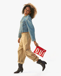 Mecca in cargo pants and a denim jacket with the Cherry Red Oui Flat Clutch w/ Tabs in her left hand