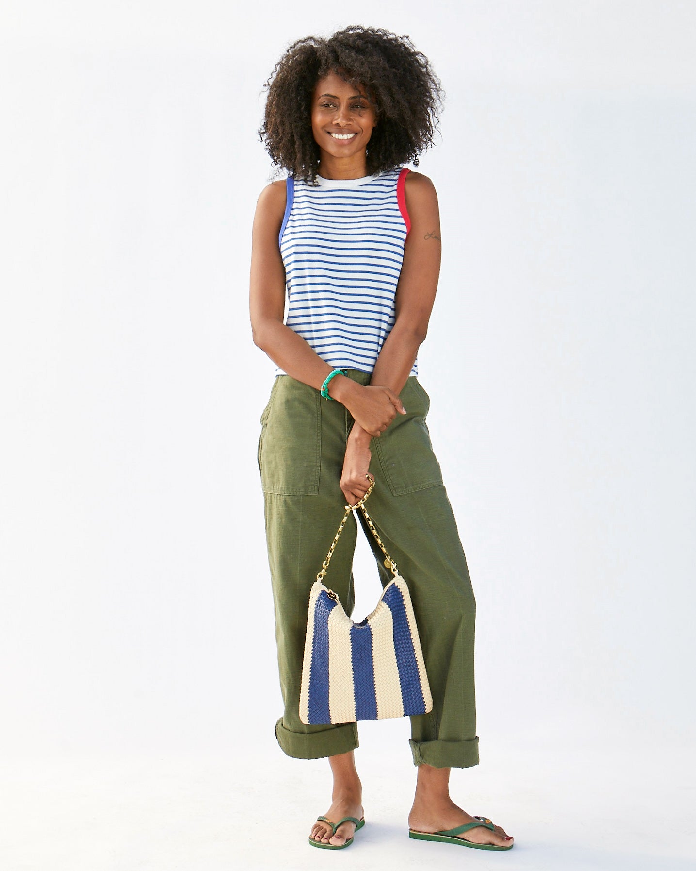 Mecca holding the Indigo & Cream Woven Racing Stripes Foldover Clutch w/ Tabs by the Box chain shoulder strap in front of her army colored pants