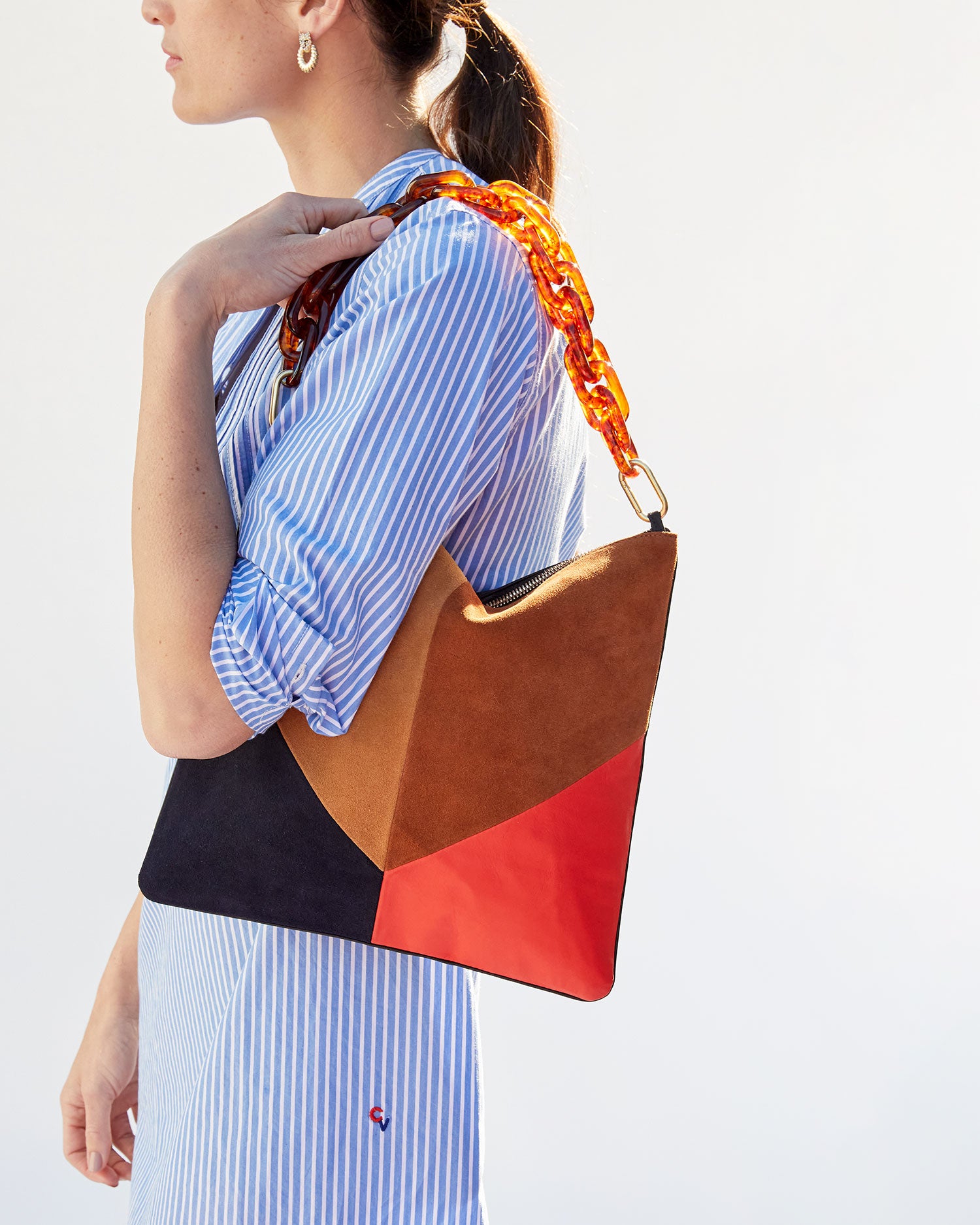 Danica holding the Suede & Nappa Patchwork Foldover Clutch with Tabs on her shoulder by the tortoise resin shortie strap 