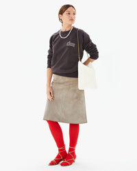 Zoe in a suede skirt , red tights and a faded black sweatshirt. She’s holding the Brie diagonal woven foldover clutch with tabs on her shoulder 