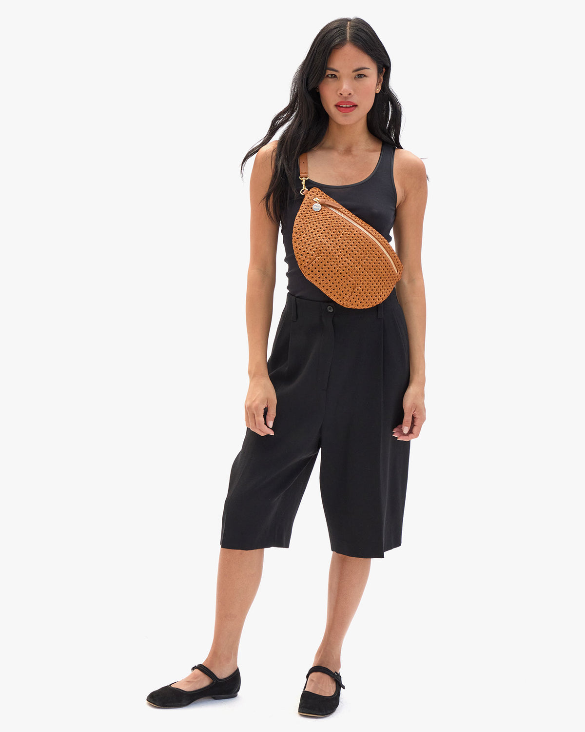 Model wearing a blank tank and black capri pants with the Tan Rattan Grande Fanny over her chest. 