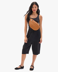 Model wearing a blank tank and black capri pants with the Tan Rattan Grande Fanny over her chest. 