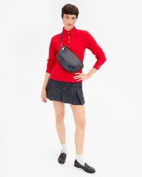 Model wearing a red long-sleeve polo shirt, a pleated mini skirt, white socks, and black leather loafers, and carrying the Twilight Diagonal Woven Grande Fanny across her chest. 