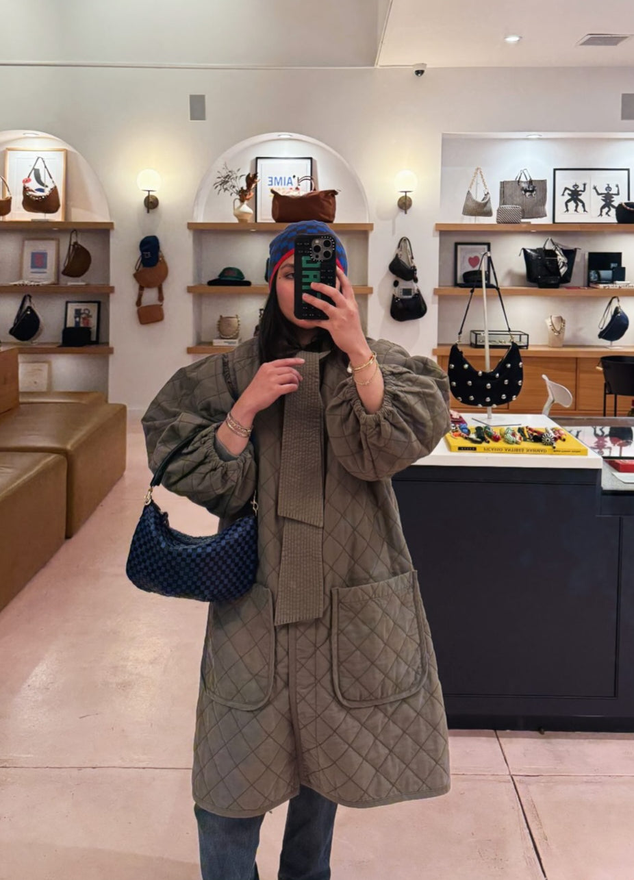 Woman taking a selfie inside of a Clare V. store while carrying the Black and Cobalt Woven Checker Petit Moyen. 