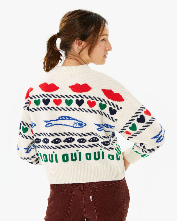 back view of Zoe wearing the Cream w/ Multi Icon Intarsia Icon Sweater with her brown pants