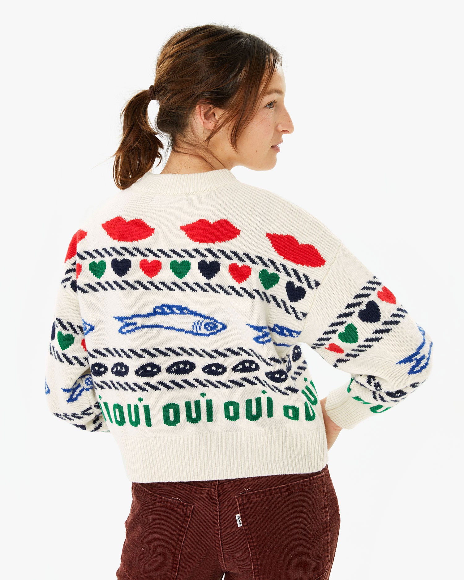 back view of Zoe wearing the Cream w/ Multi Icon Intarsia Icon Sweater with her brown pants