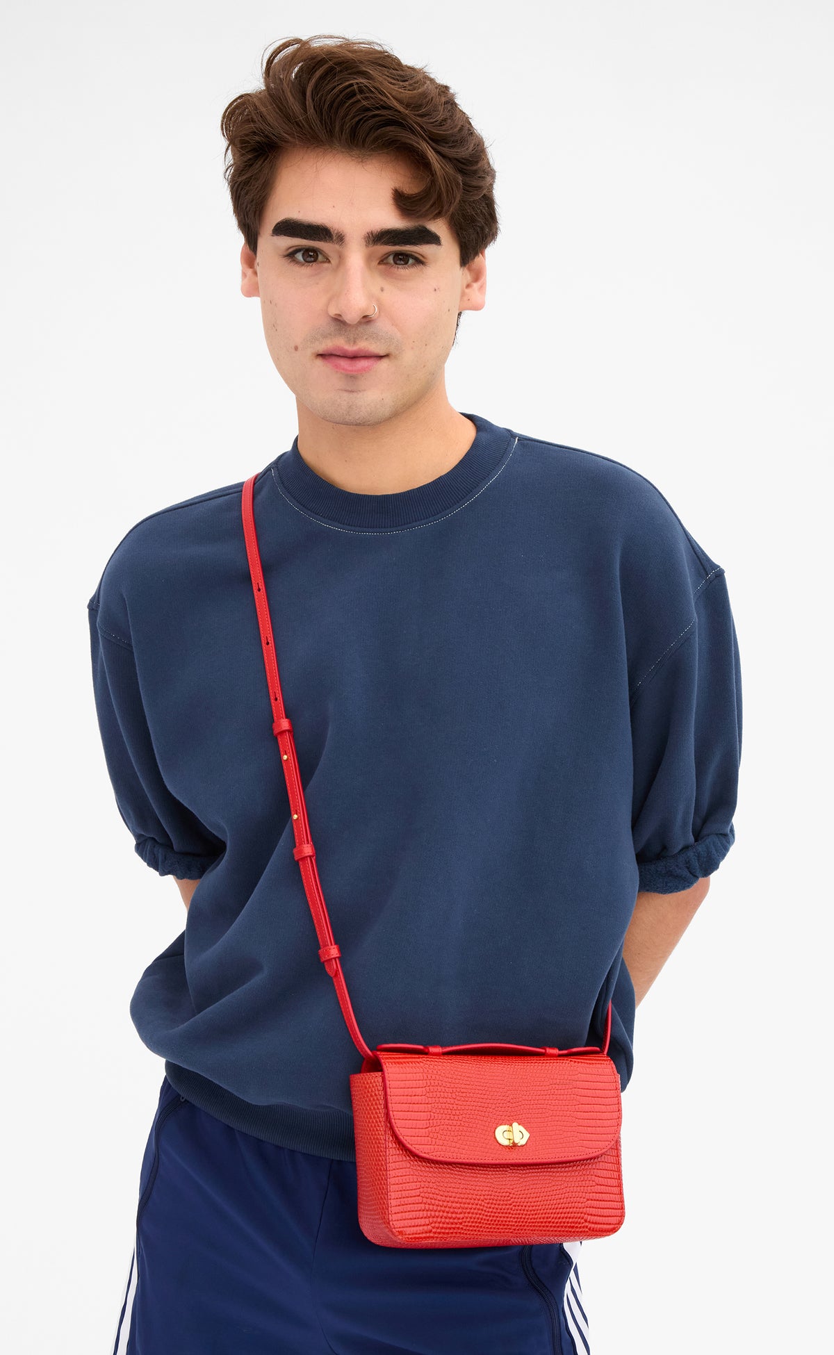 Male model wearing the Navy Short Sleeve Oversized Sweatshirt and carrying the Red Embossed Lizard Kathryn as a crossbody bag. 